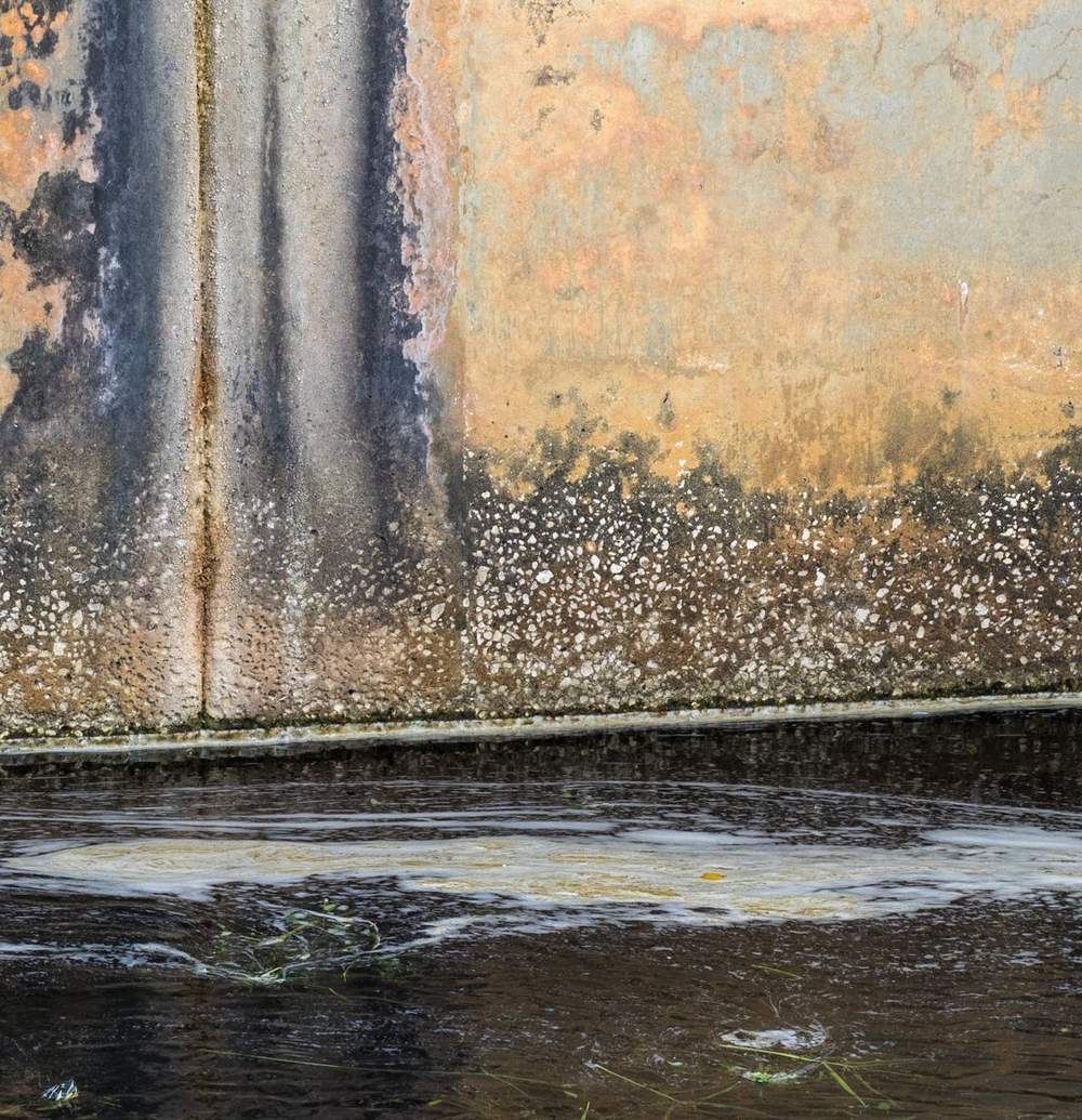 Water stain running down a joint in a concrete wall into standing water at its base