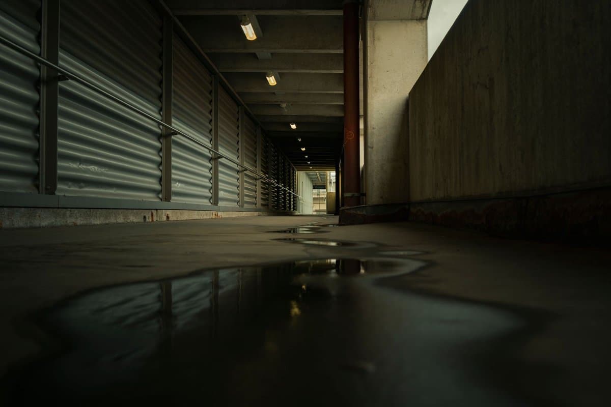 Puddle on the concrete floor of a dim parkade walkway lined with concrete walls
